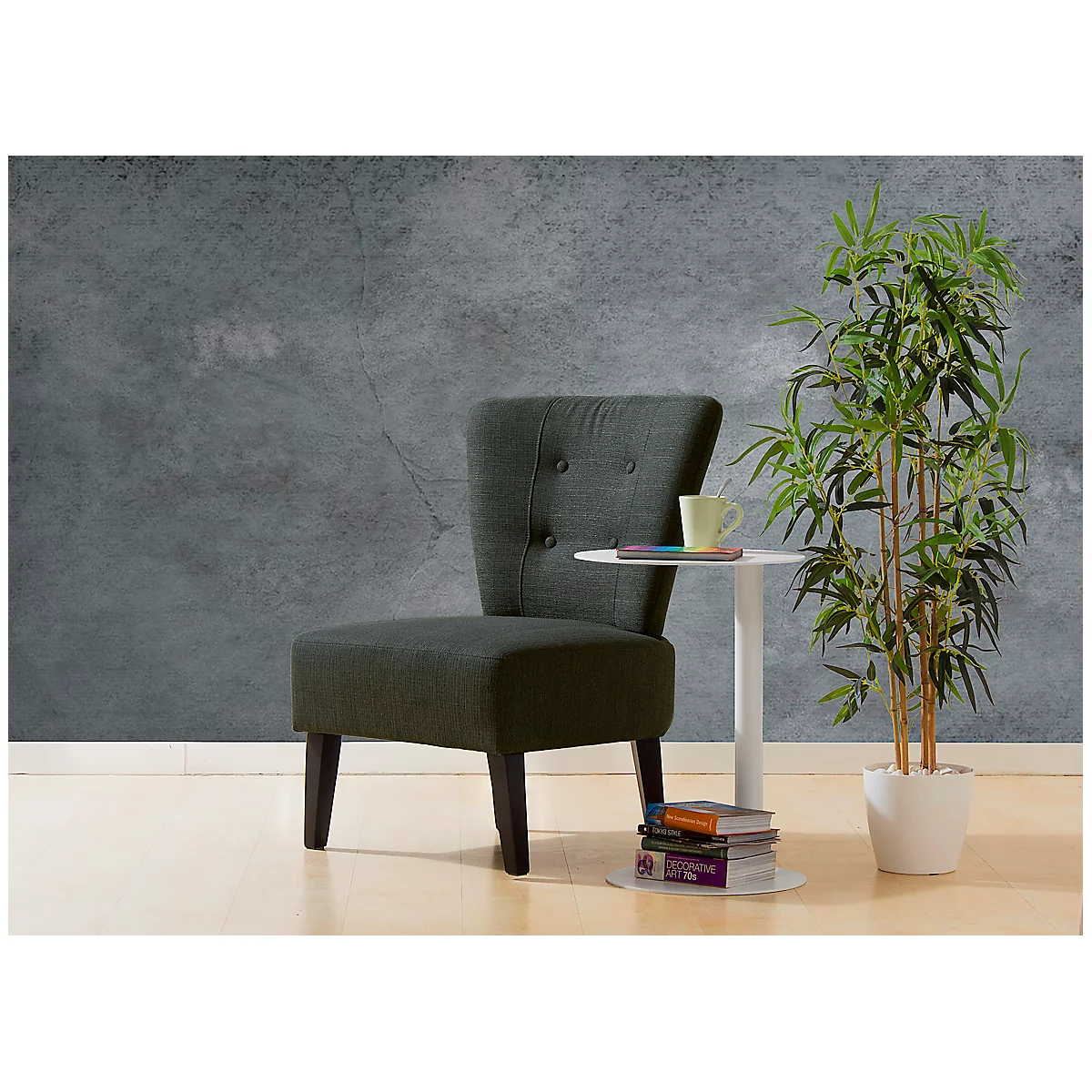 Dunkelgrauer Sessel neben kleinem Tisch mit Büchern und einer Tasse. Daneben Bambuspflanze.