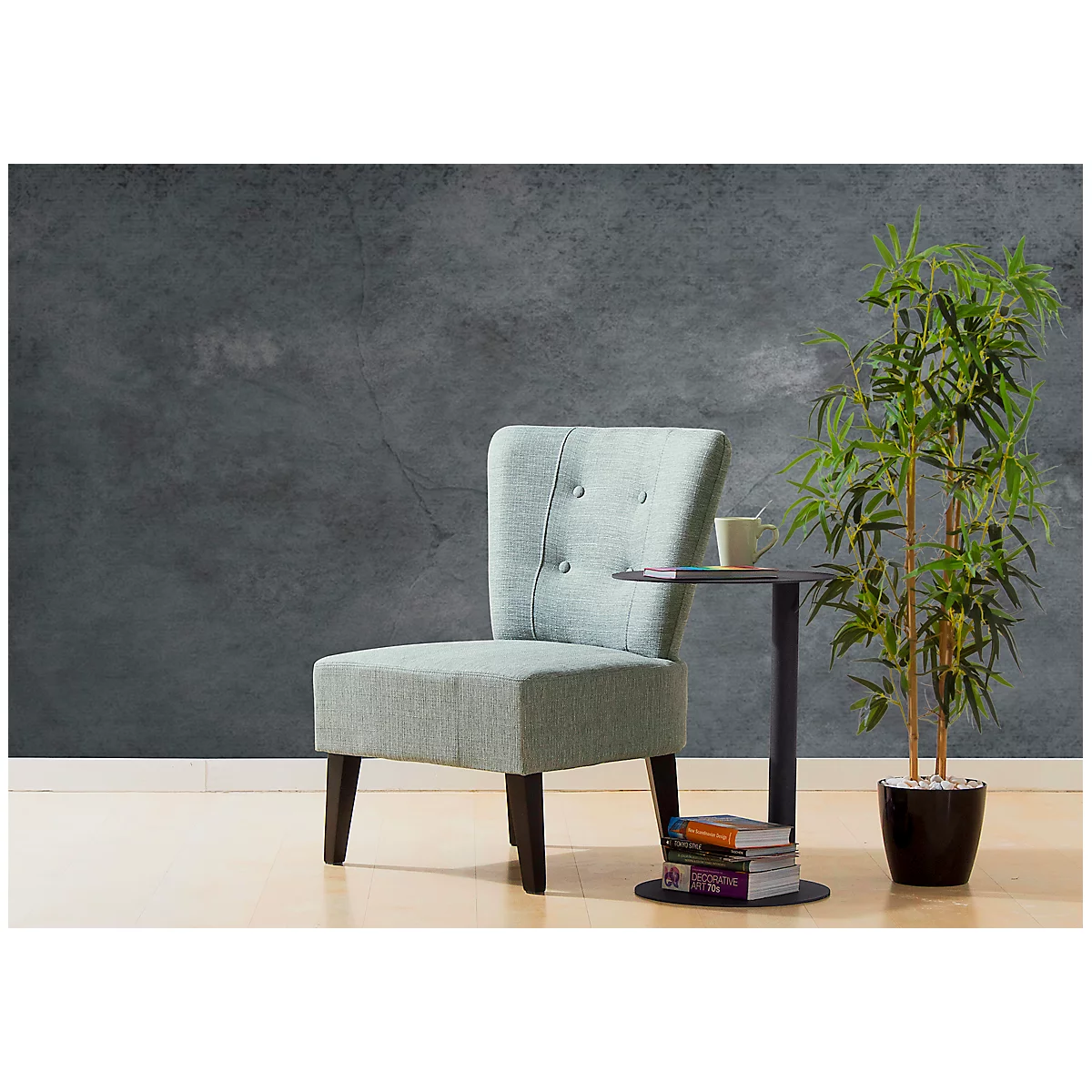 Lichtblauwe fauteuil naast een bijzettafel met een kopje, daarnaast een plant voor een grijze muur.