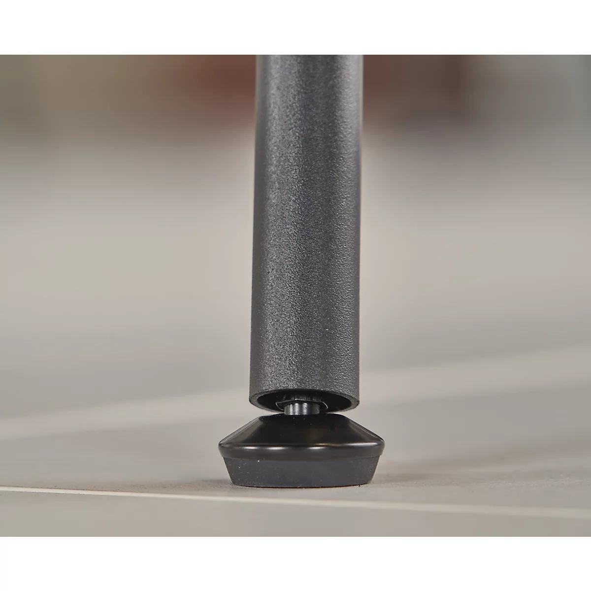 Gros plan d'un pied de meuble noir reposant sur une surface claire. Le pied est cylindrique, la partie inférieure est conique.