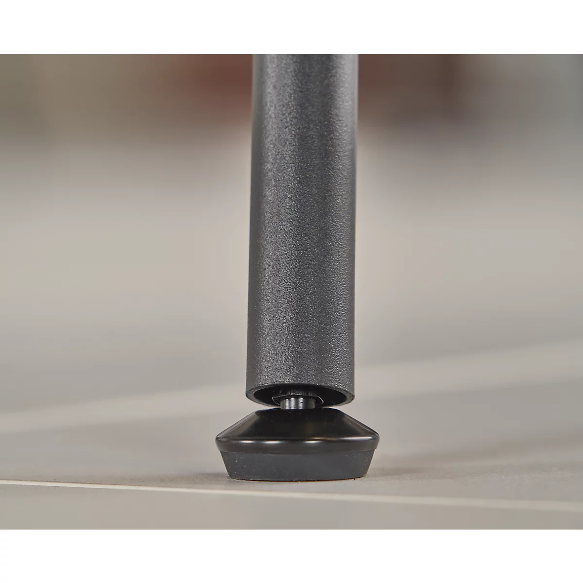 Gros plan d'un pied de table. La jambe grise repose sur un pied noir de forme conique.