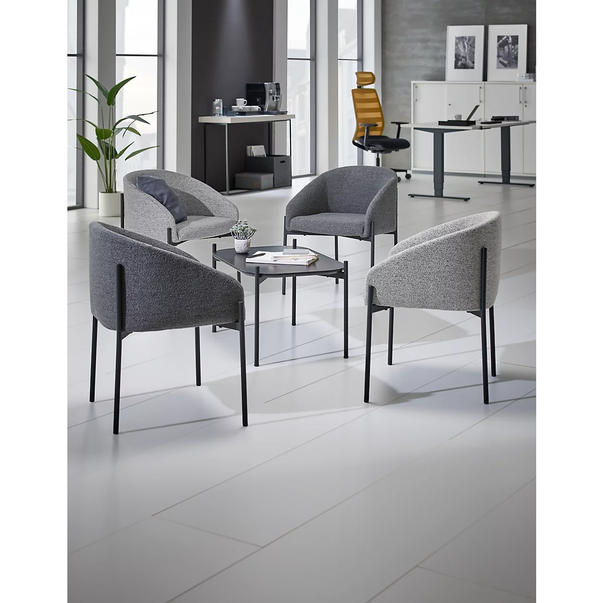 Grijze loungehoek met vier stoelen en een tafel. De achtergrond toont een bureau en een raam.