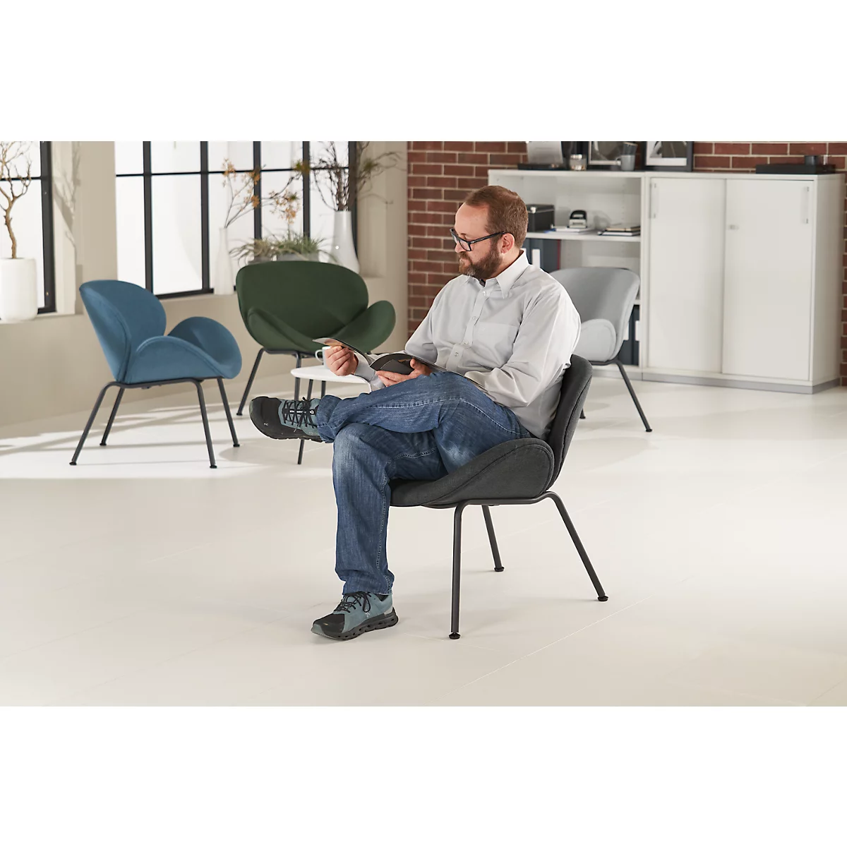 Mann sitzt entspannt in einem grauen Designerstuhl. Im Hintergrund weitere Stühle und Möbel.