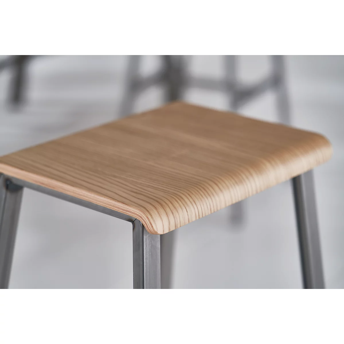 Stool with wooden top. Grainy plate, rounded edges. Metal legs, close-up.
