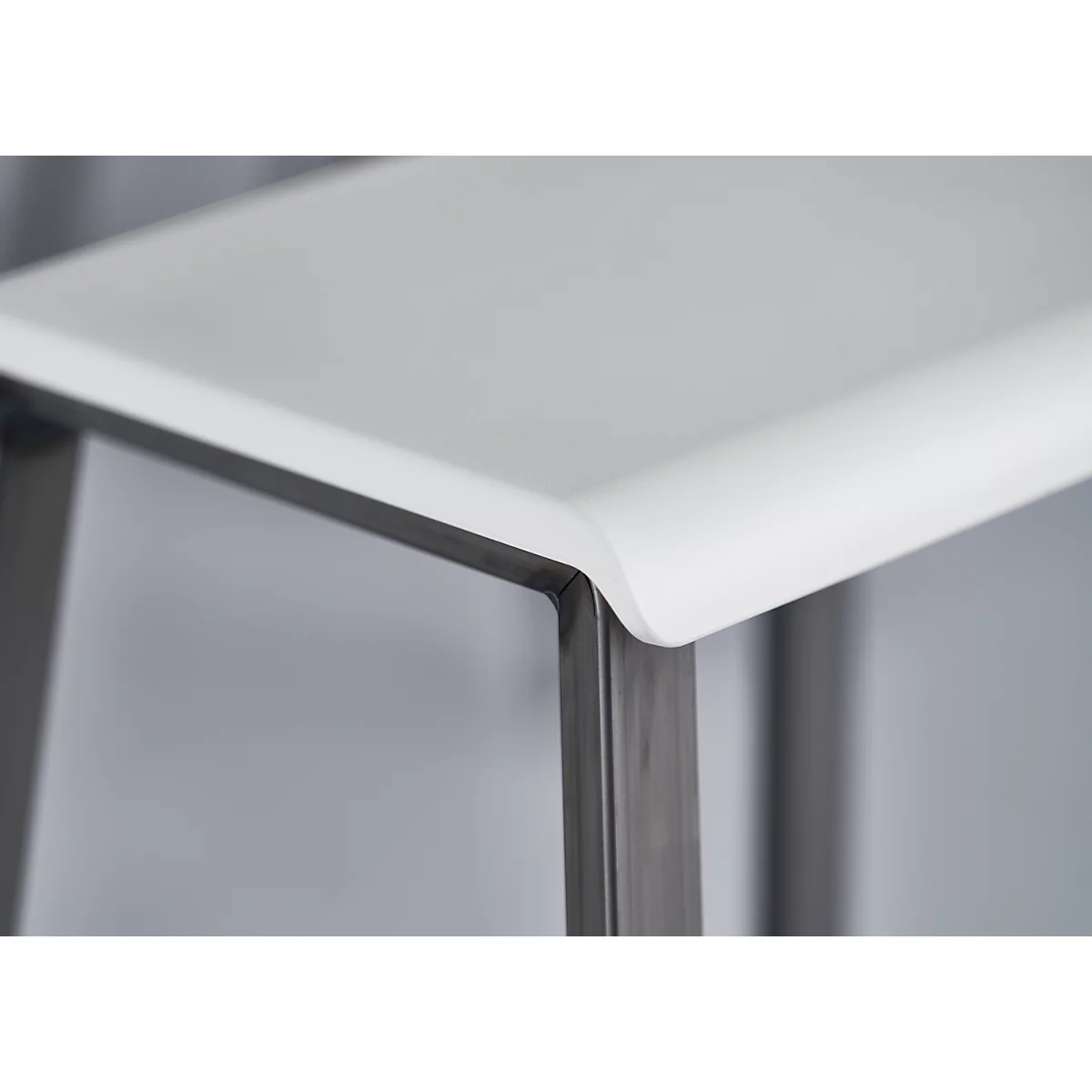 Close-up of a table edge with rounded white surfaces and metal frame. The edge is smooth and modern in design.