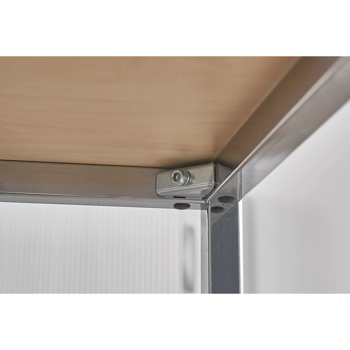 Close-up of table legs and table top. Metal corner connector with screw on light brown wooden board.