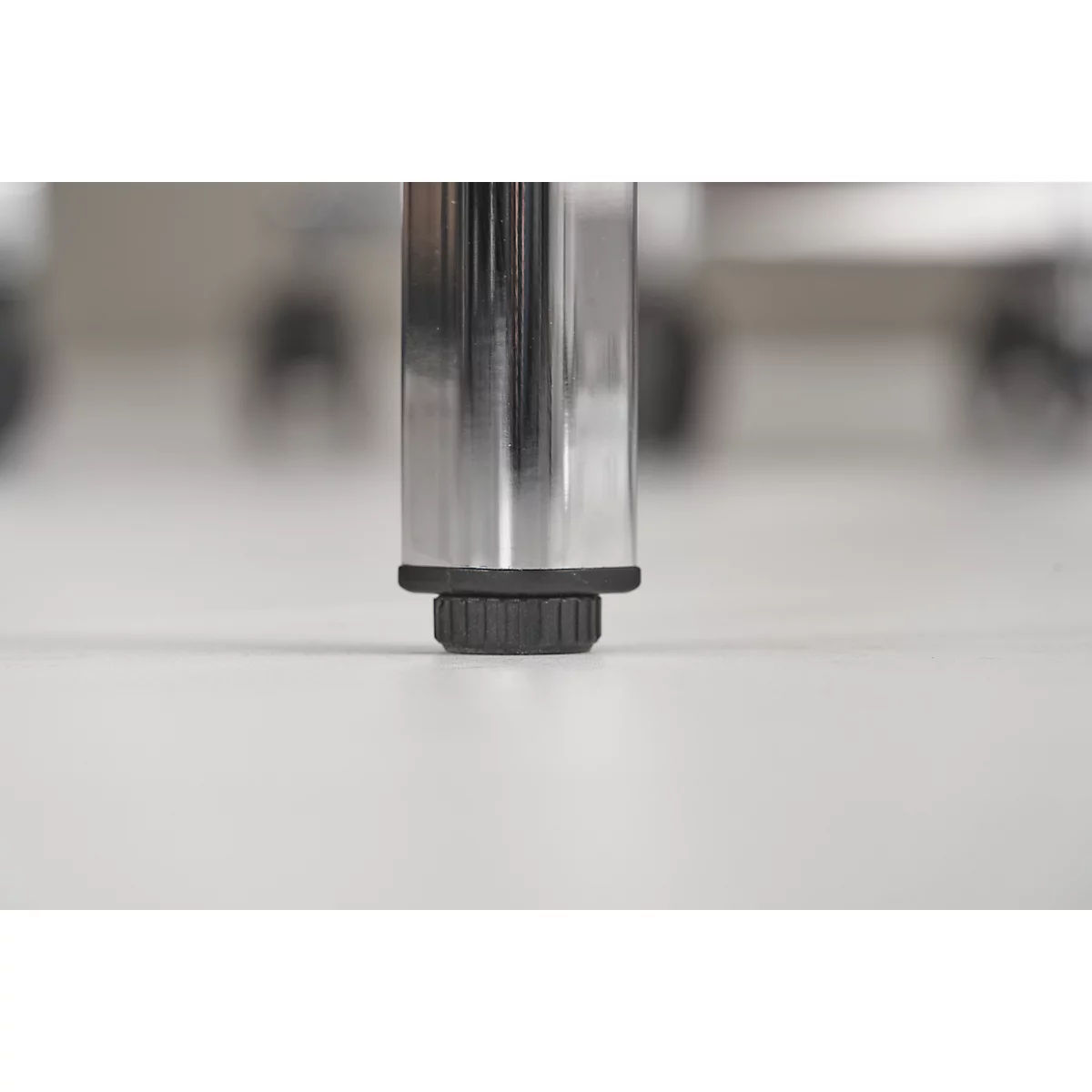 Close-up of a chair leg standing on a white surface. The leg is made of polished metal with a black foot.