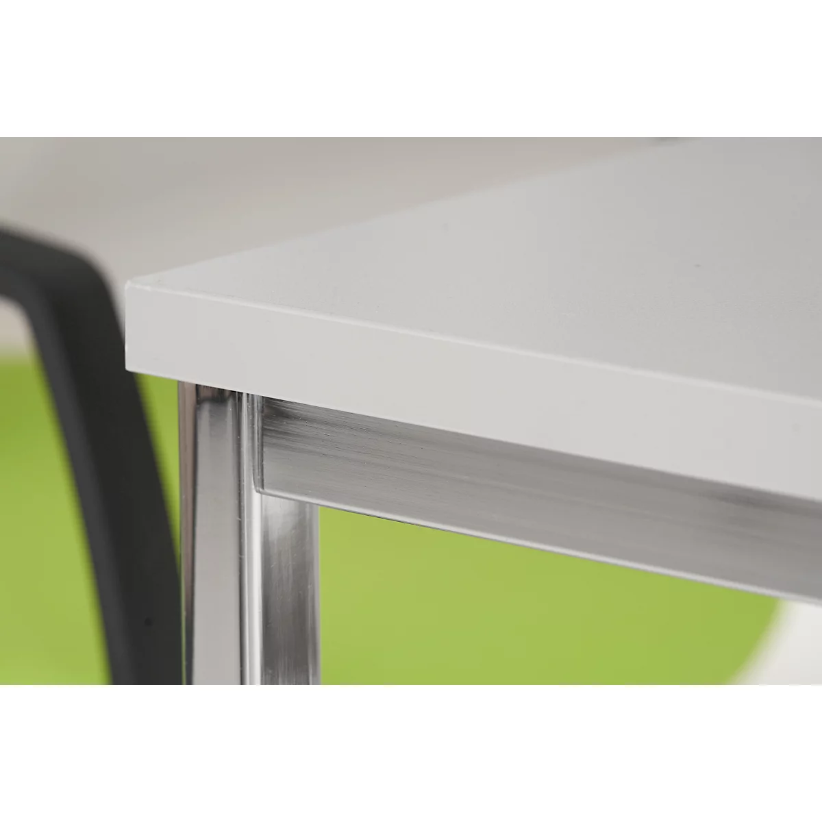 Close-up: White table top with metal legs and green background, part of a chair visible.