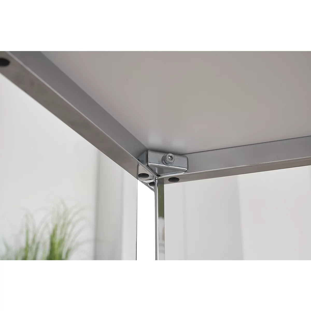 Close-up: Corner of a table, silver metal frame, white tabletop material, screws and connections.