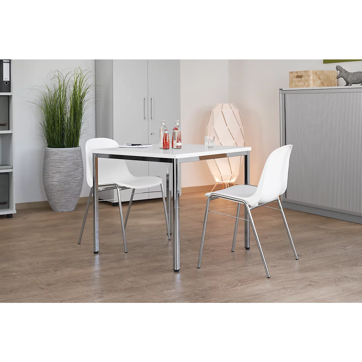 White table and chairs in modern office. A vase with tall ornamental grass in front. Drinks are on the table.