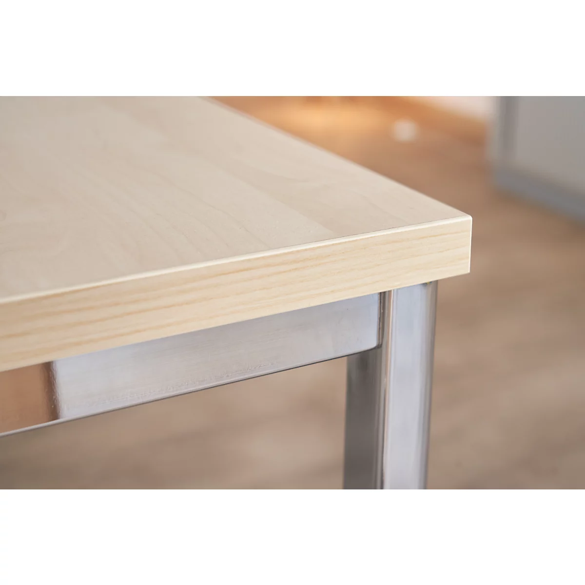 Primer plano de una mesa de madera clara, sobre una pata de color plateado.