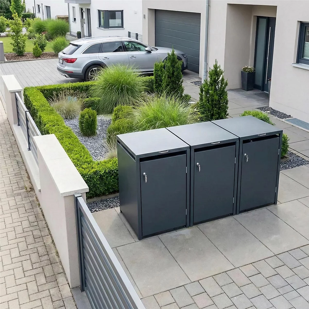 Drie grijze vuilnisbakken staan voor een huis met een tuin en een auto.