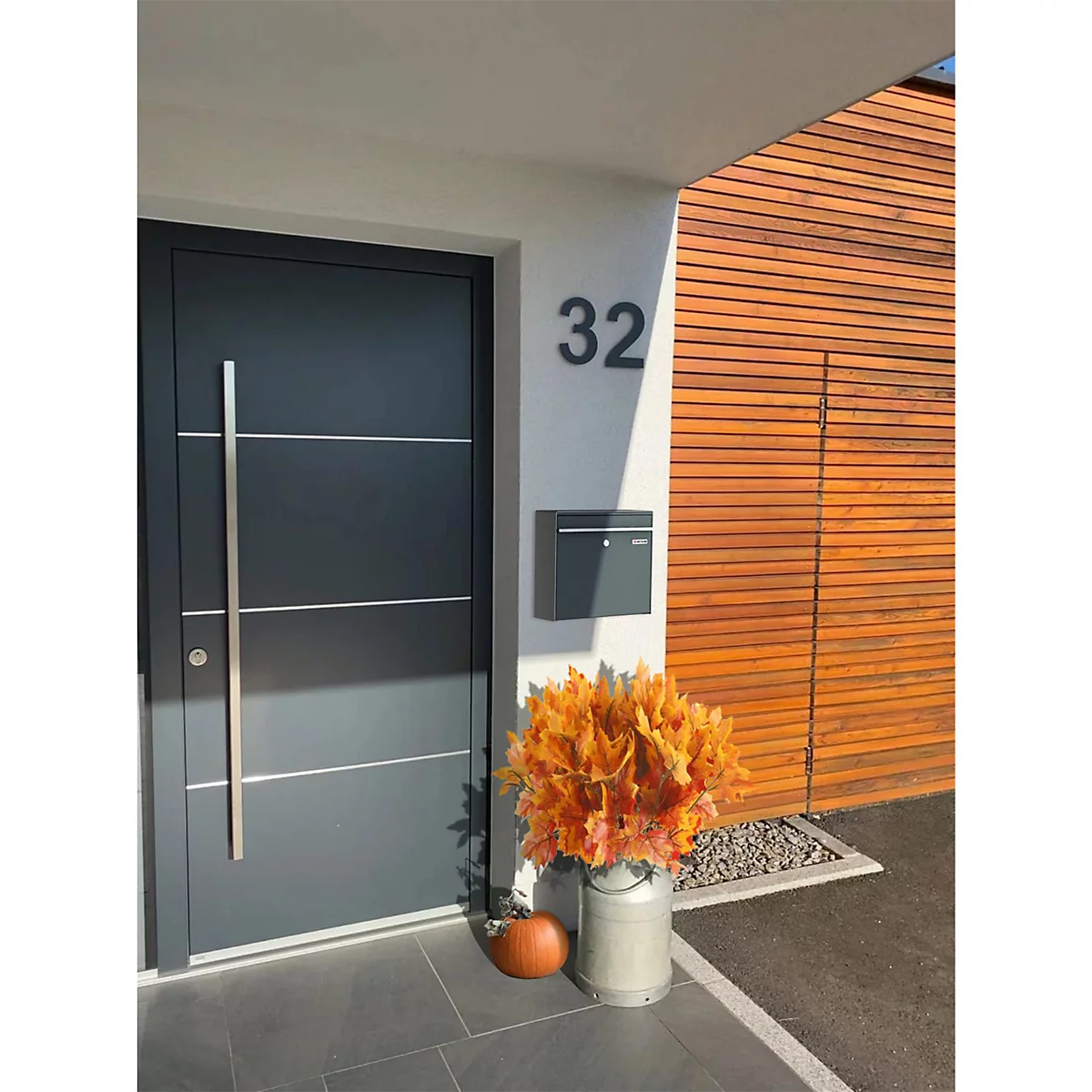 Porte d'entrée grise avec poignée en acier inoxydable et numéro de maison 32. Citrouille et décorations d'automne devant.