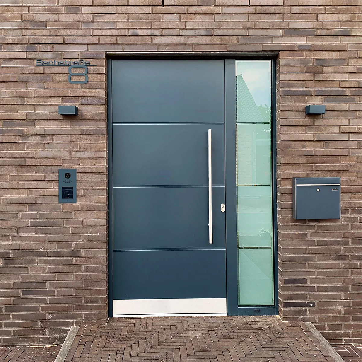 Porte d'entrée anthracite moderne avec section vitrée et numéro 8 sur mur de briques.