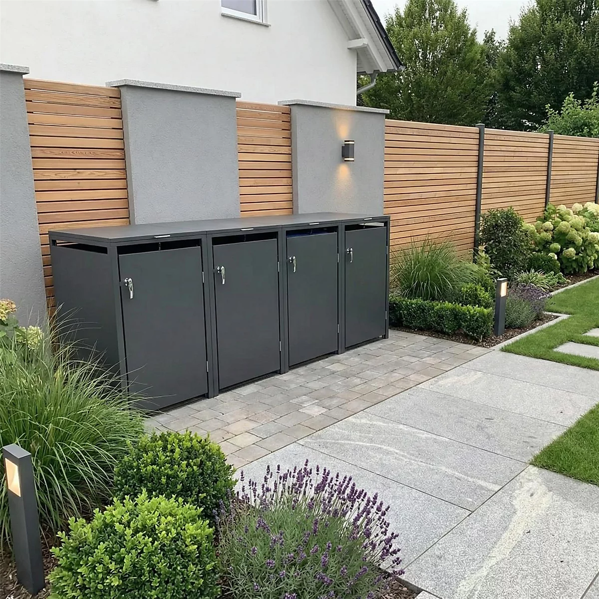 Coffre à ordures gris devant une clôture à lattes en bois. Devant, un jardin avec des plantes et un chemin. Maison en arrière-plan.