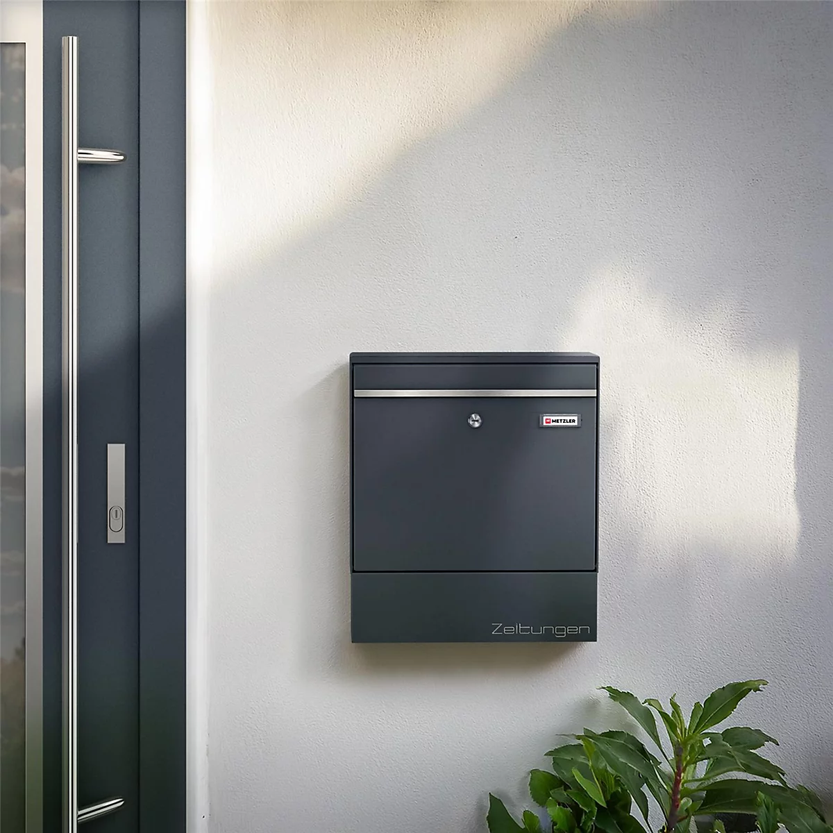 Dunkelgrauer Briefkasten an Hauswand. Unterhalb steht "Zeitungen".