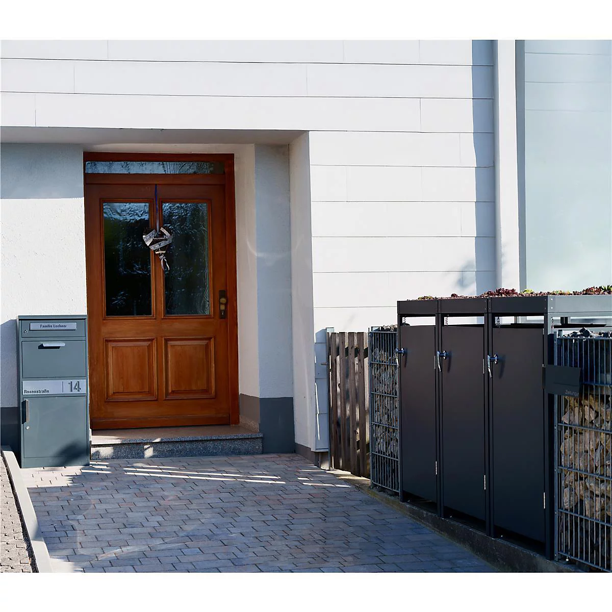 Porte en bois avec clés, boîte aux lettres grise, poubelles modernes devant une maison.