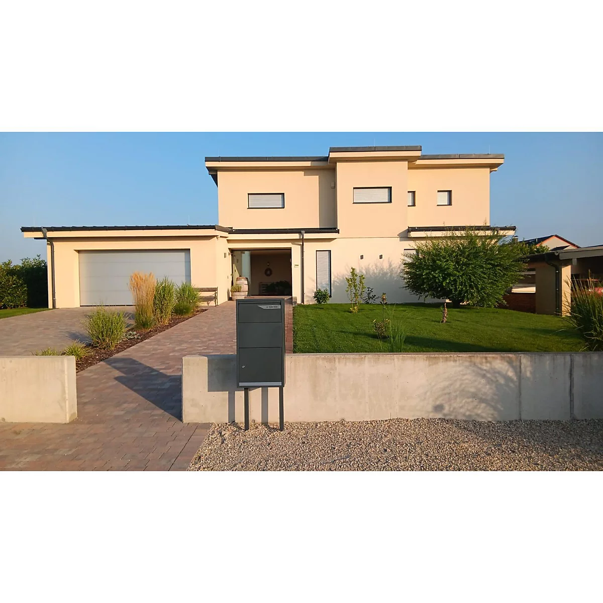 Moderne Villa mit Briefkasten, Rasen und Auffahrt. Hellblauer Himmel im Hintergrund.