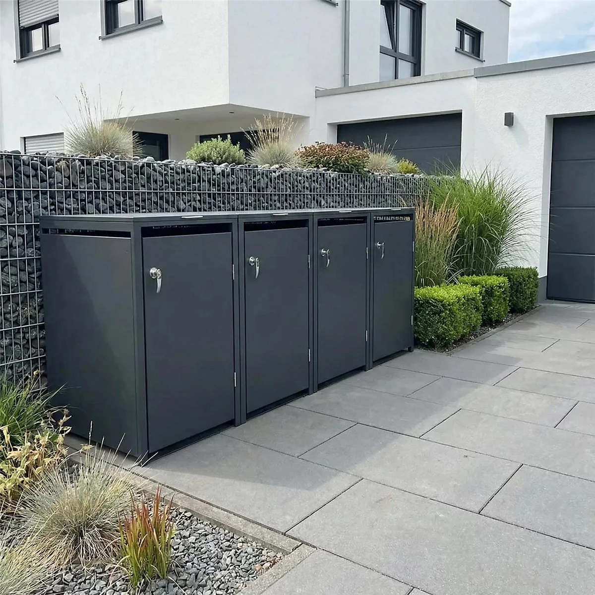 Donkergrijze vuilnisbakken in een geplaveide oprit voor een modern huis.