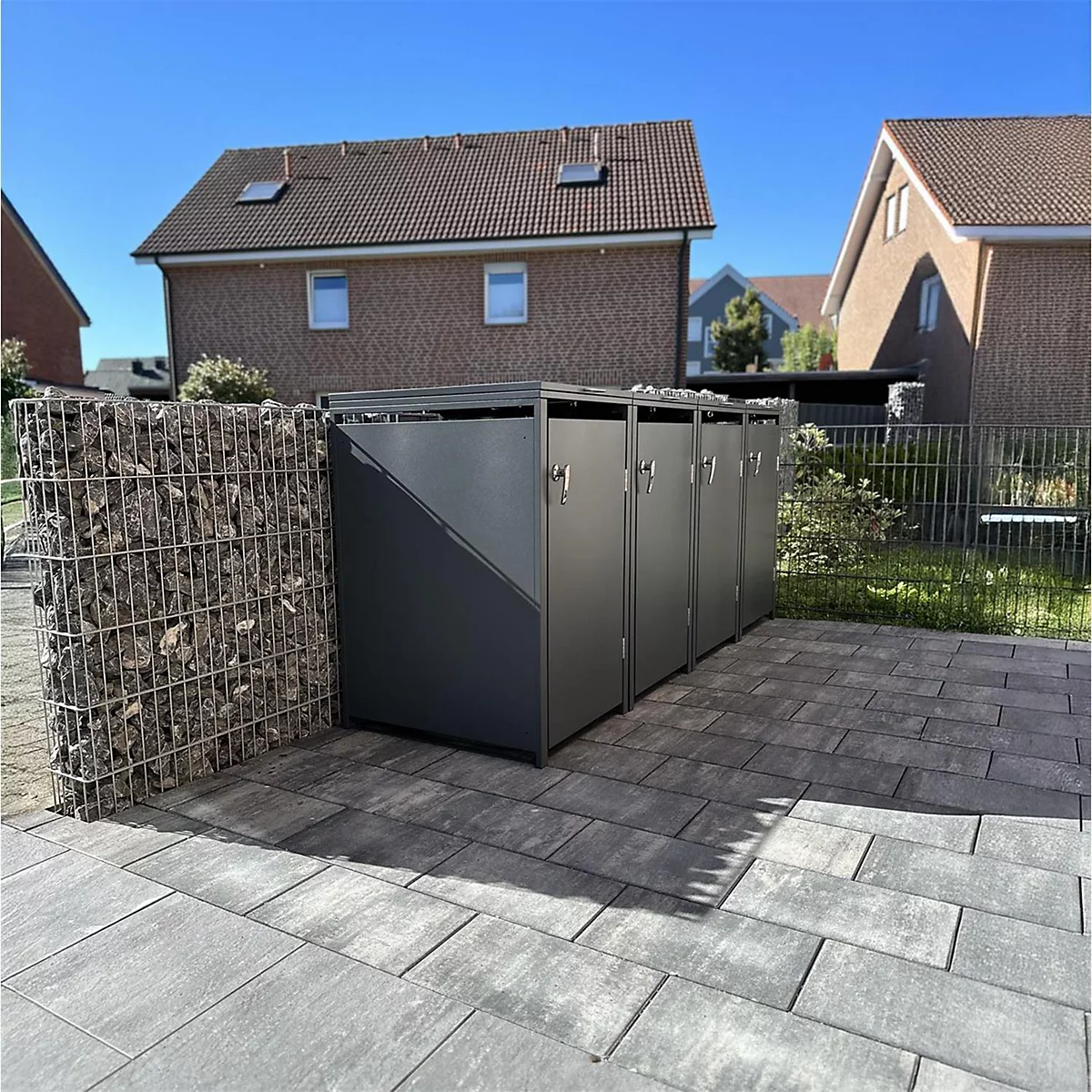 Donkere afvalbakken op stenen platen voor woongebouwen, links een stenen muur.