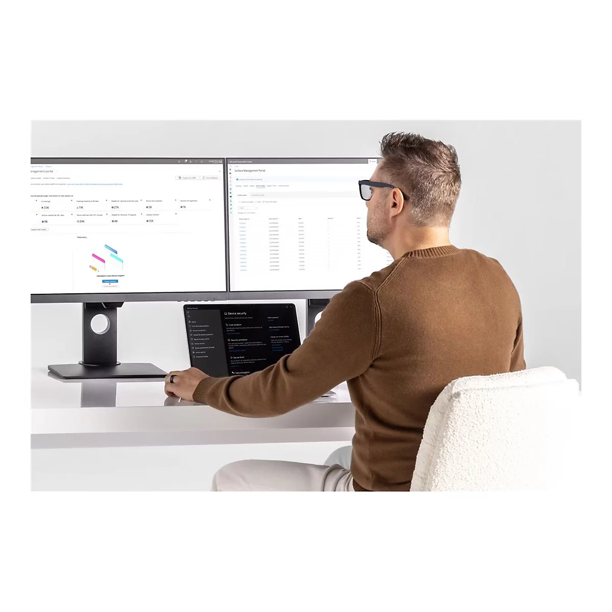 Ein Mann mit Brille sitzt am Schreibtisch und arbeitet an einem Computer. Auf dem Tisch stehen zwei Monitore und ein Laptop.