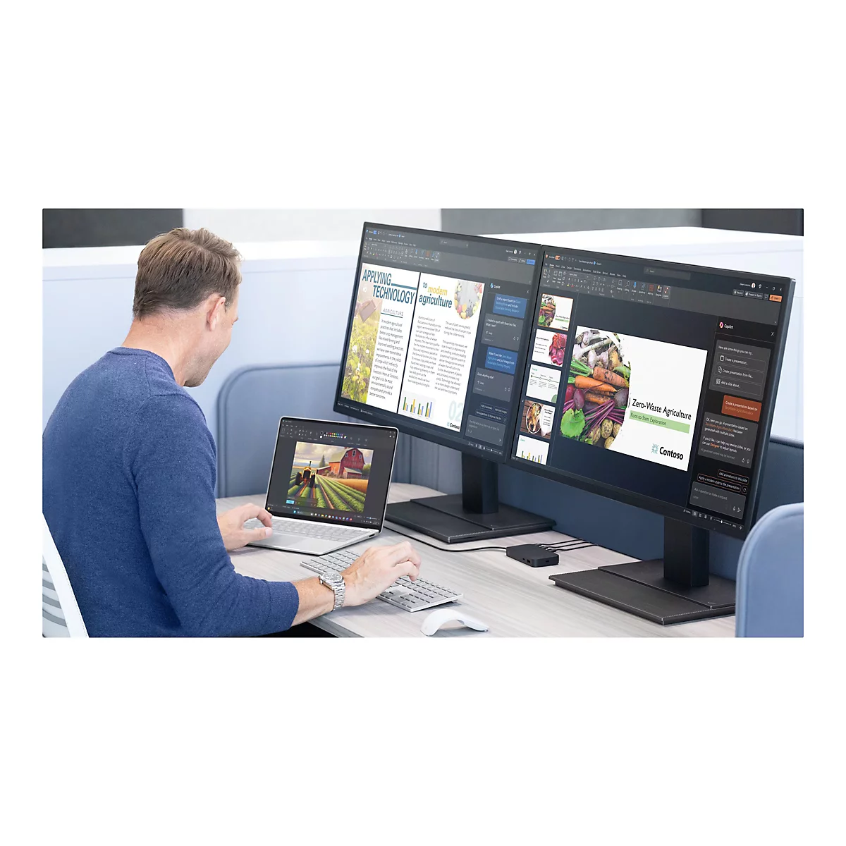 Mann sitzt an einem Schreibtisch und arbeitet an zwei Monitoren und einem Laptop. Auf dem Bildschirm sind Dokumente und ein Bauernhof zu sehen.