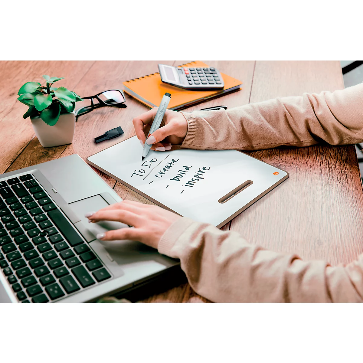 Une personne écrit avec un stylo sur un bloc-notes, un ordinateur portable et d'autres accessoires sur une table en bois.