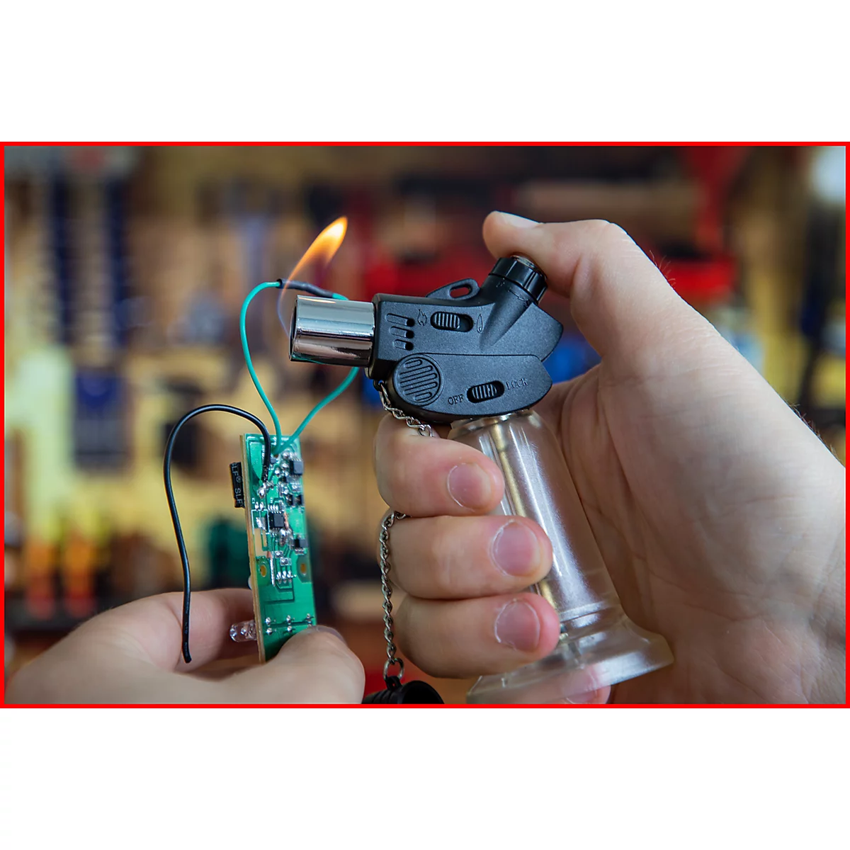 Person hält eine Lötlampe mit Feuer. Eine Platine ist mit Drähten angeschlossen.