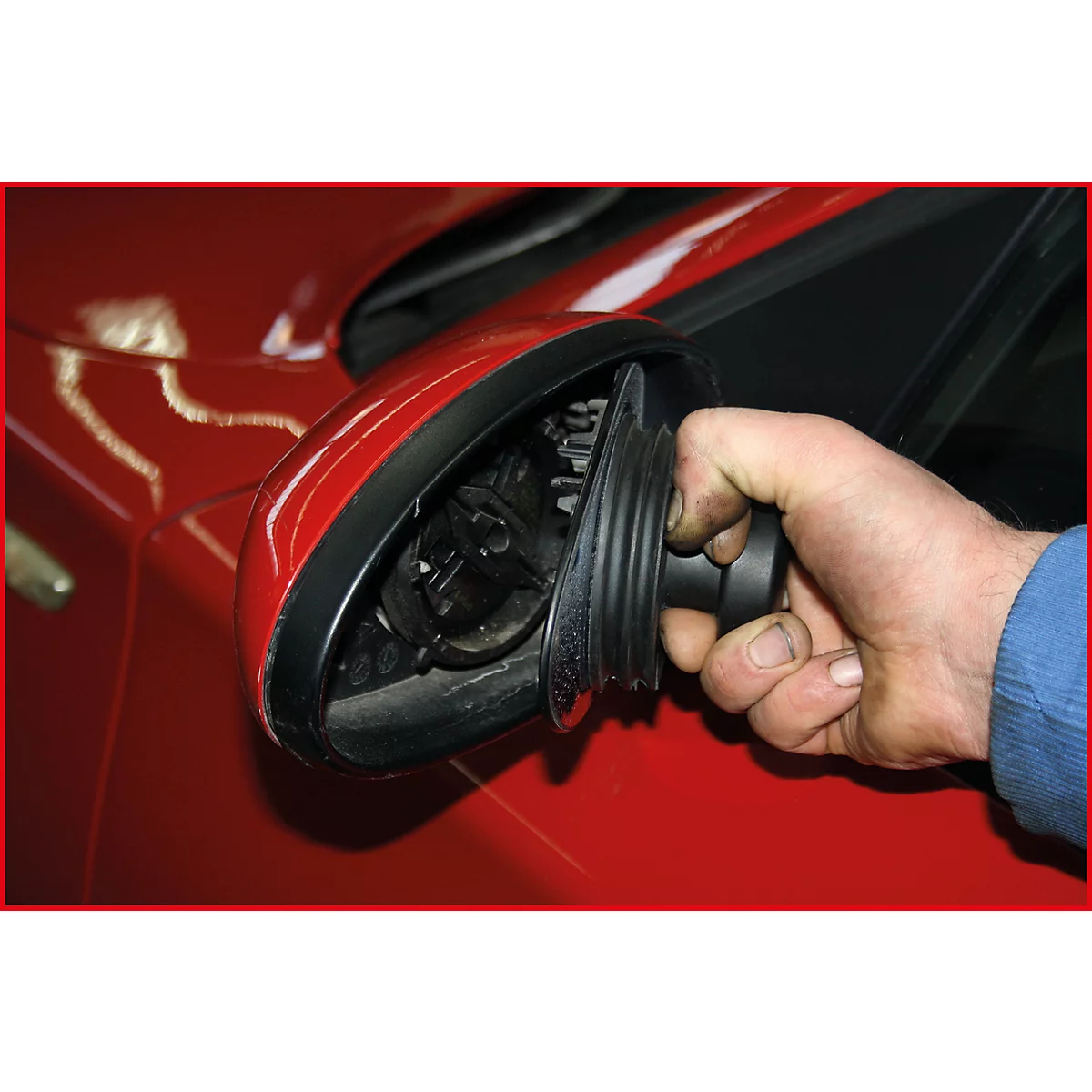 Ein Mann hält ein schwarzes Teil eines roten Autos.