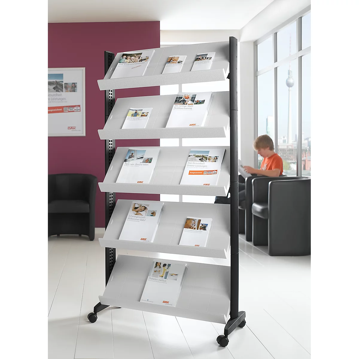 Presentation stand with brochures, behind it a boy is reading a magazine.