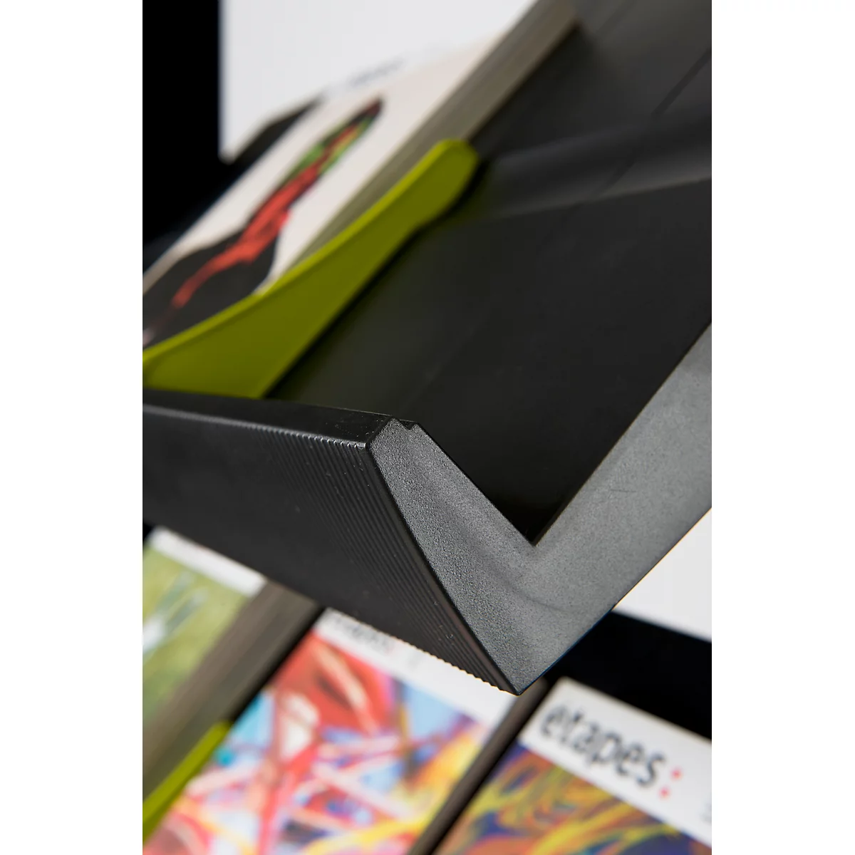 Black book stand with magazines. The top magazine shows a green page and a red illustration. The inscription "etapes:" can be seen at the bottom.