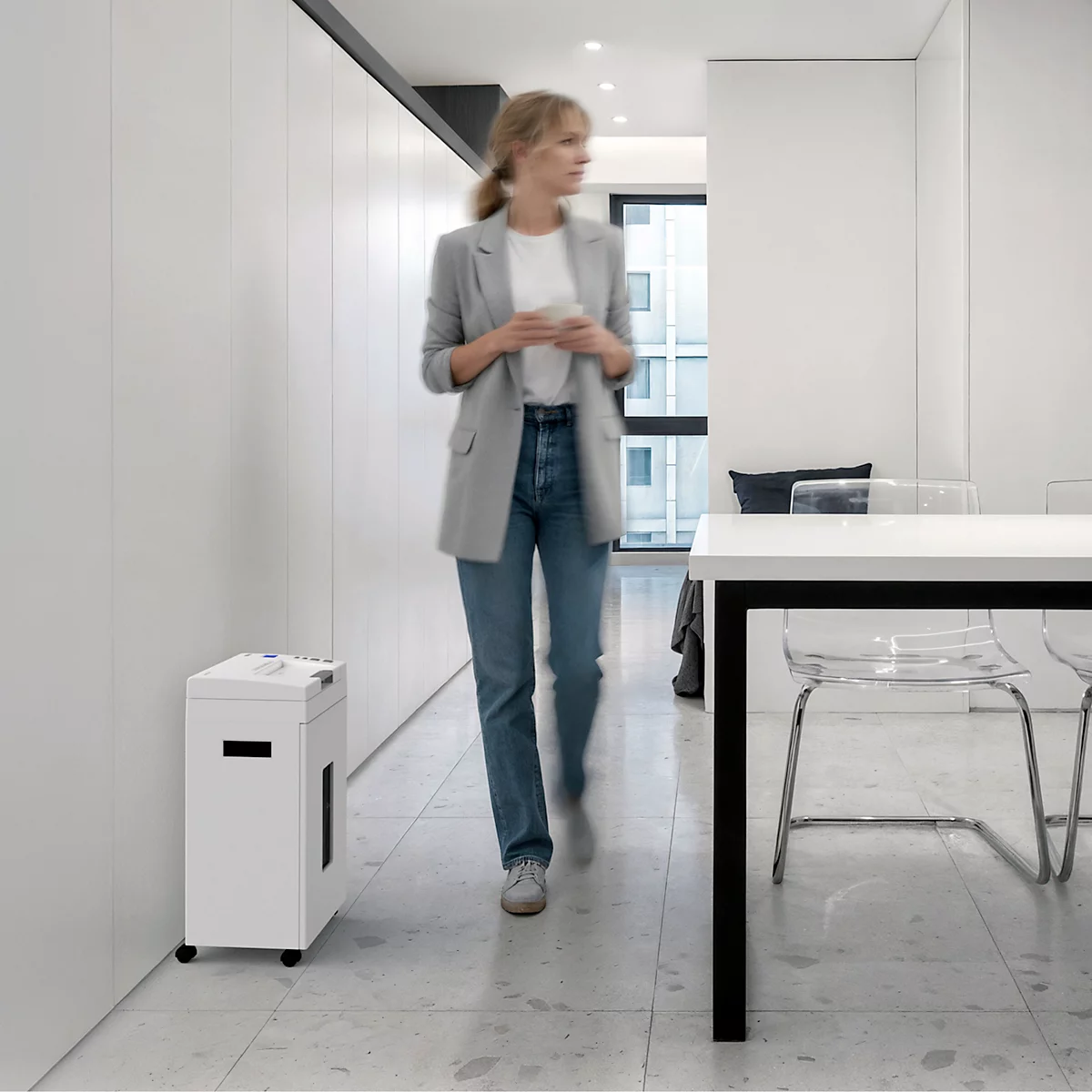 A woman walks past a paper shredder in a modern office.