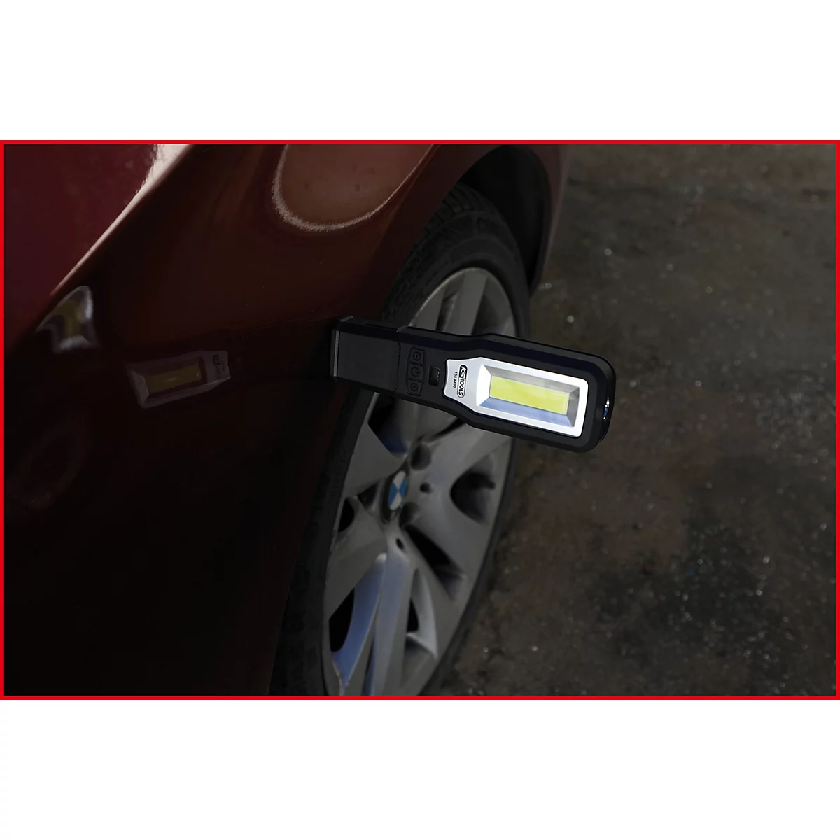 Eine schwarze LED-Arbeitsleuchte ist an einem roten Autokotflügel befestigt. Im Hintergrund ist ein Reifen und die Felge zu sehen.