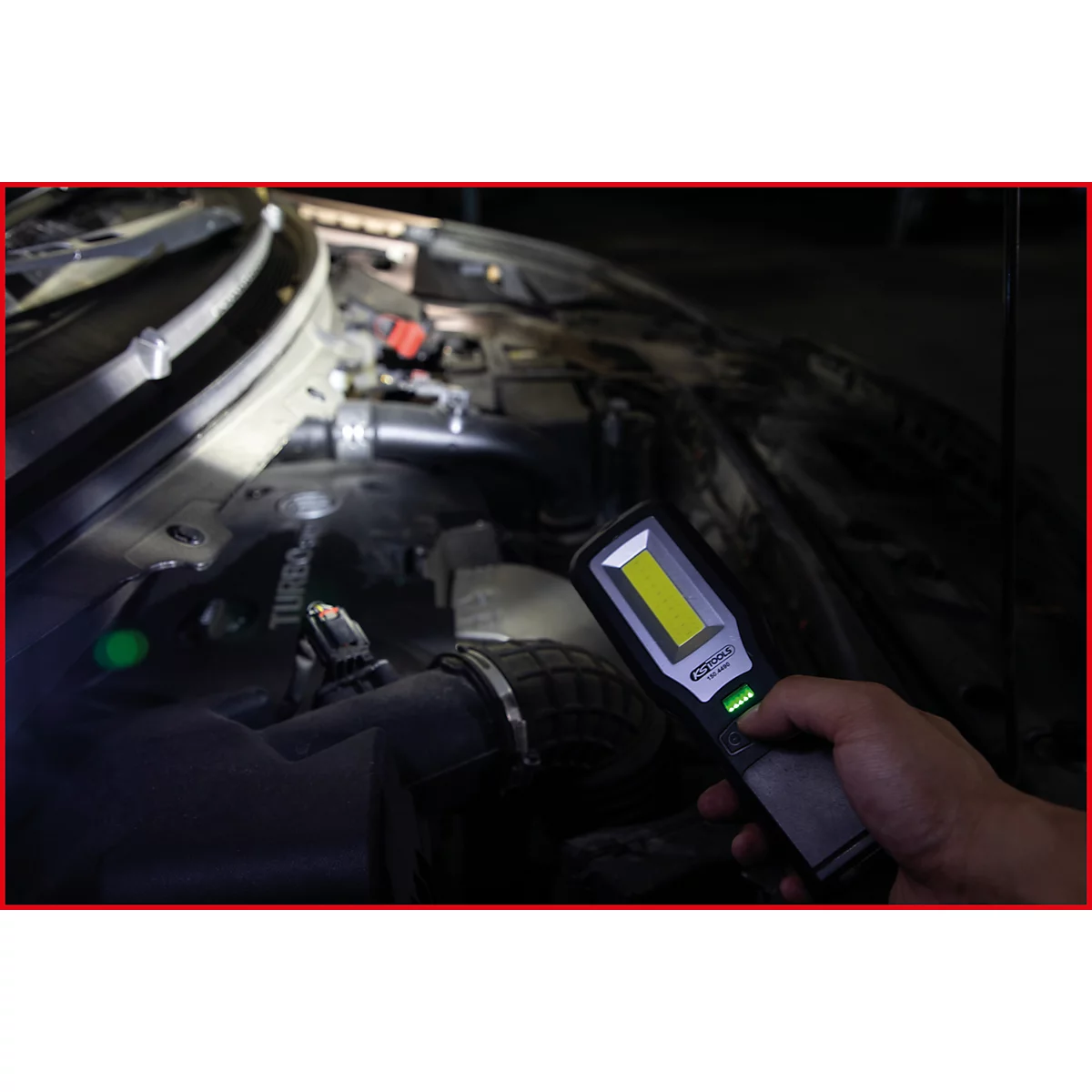Nahaufnahme einer Hand, die eine Stablampe im Motorraum eines Autos hält. Die Lampe leuchtet das Innere aus.
