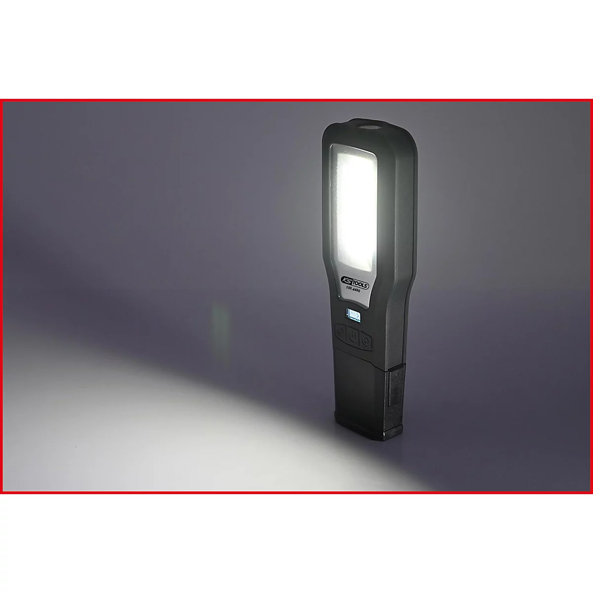 Eine schwarze LED-Werkstattlampe leuchtet hell. Sie steht auf einer schrägen Fläche. Ein weißer Lichtkegel wird auf eine graue Oberfläche geworfen.