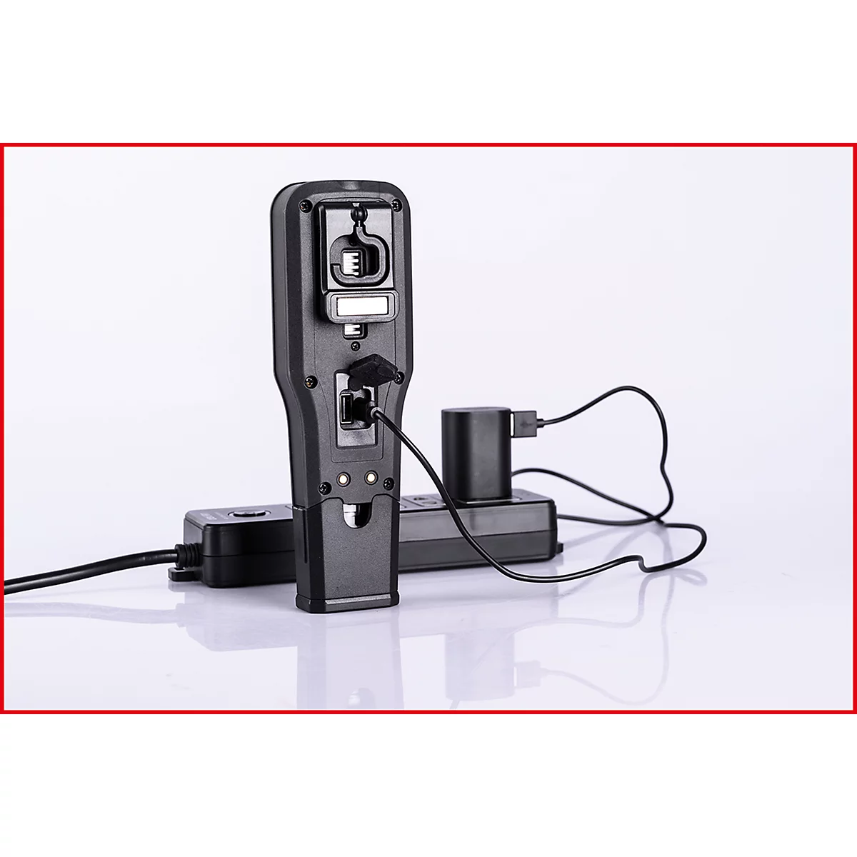Ein schwarzes mobiles Gerät steht mit Ladegerät vor weißem Hintergrund. Kabel sind angeschlossen.
