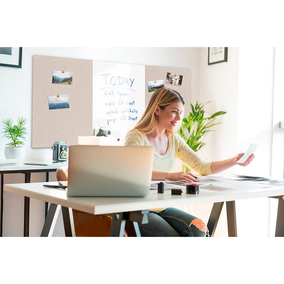 Une femme souriante est assise à un bureau avec un ordinateur portable et des photos qu'elle regarde.