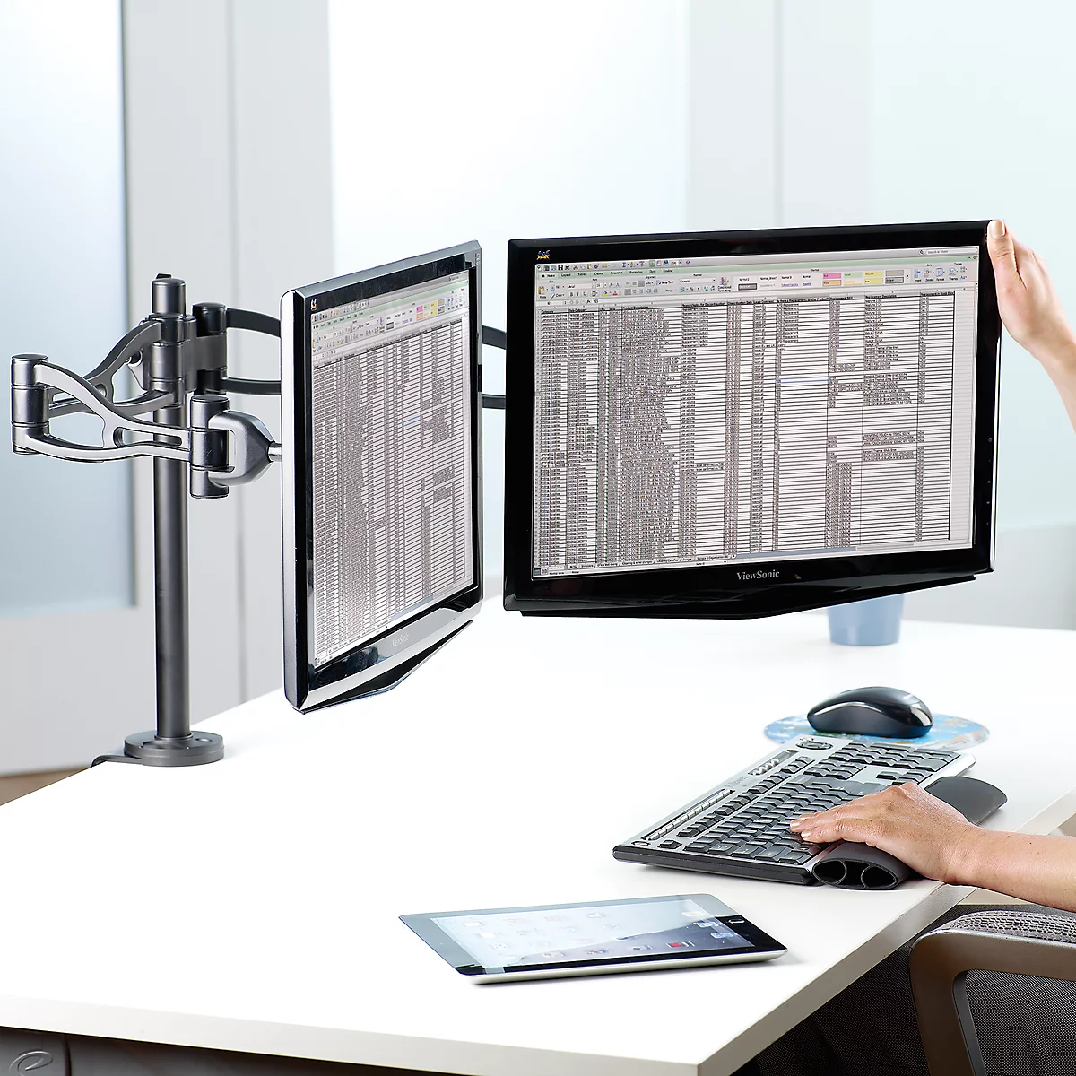 Double monitor stand on desk. Two screens with tables. Next to it mouse, keyboard and tablet.