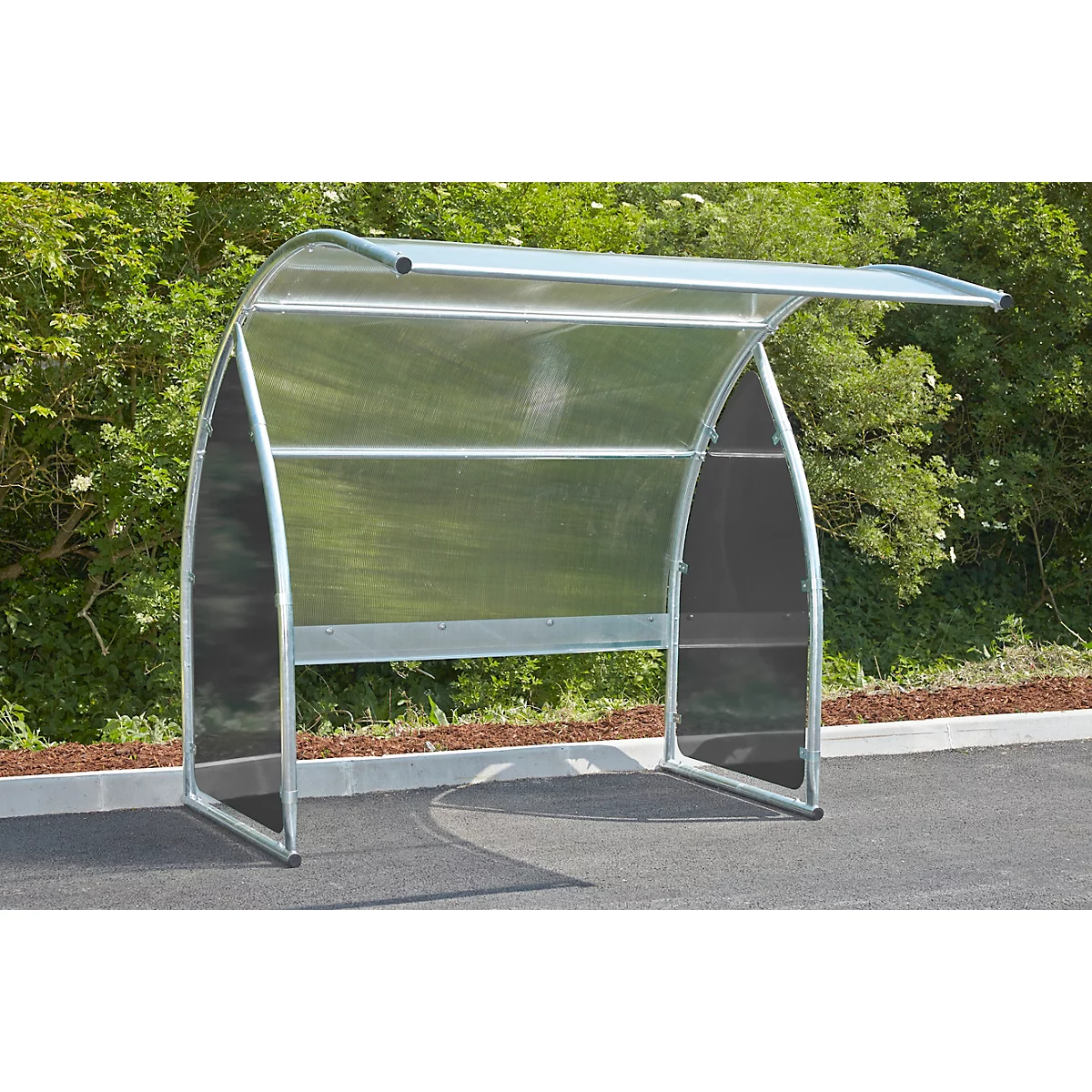 Metal bike shelter with plexiglass walls and roof, in front of green bushes.