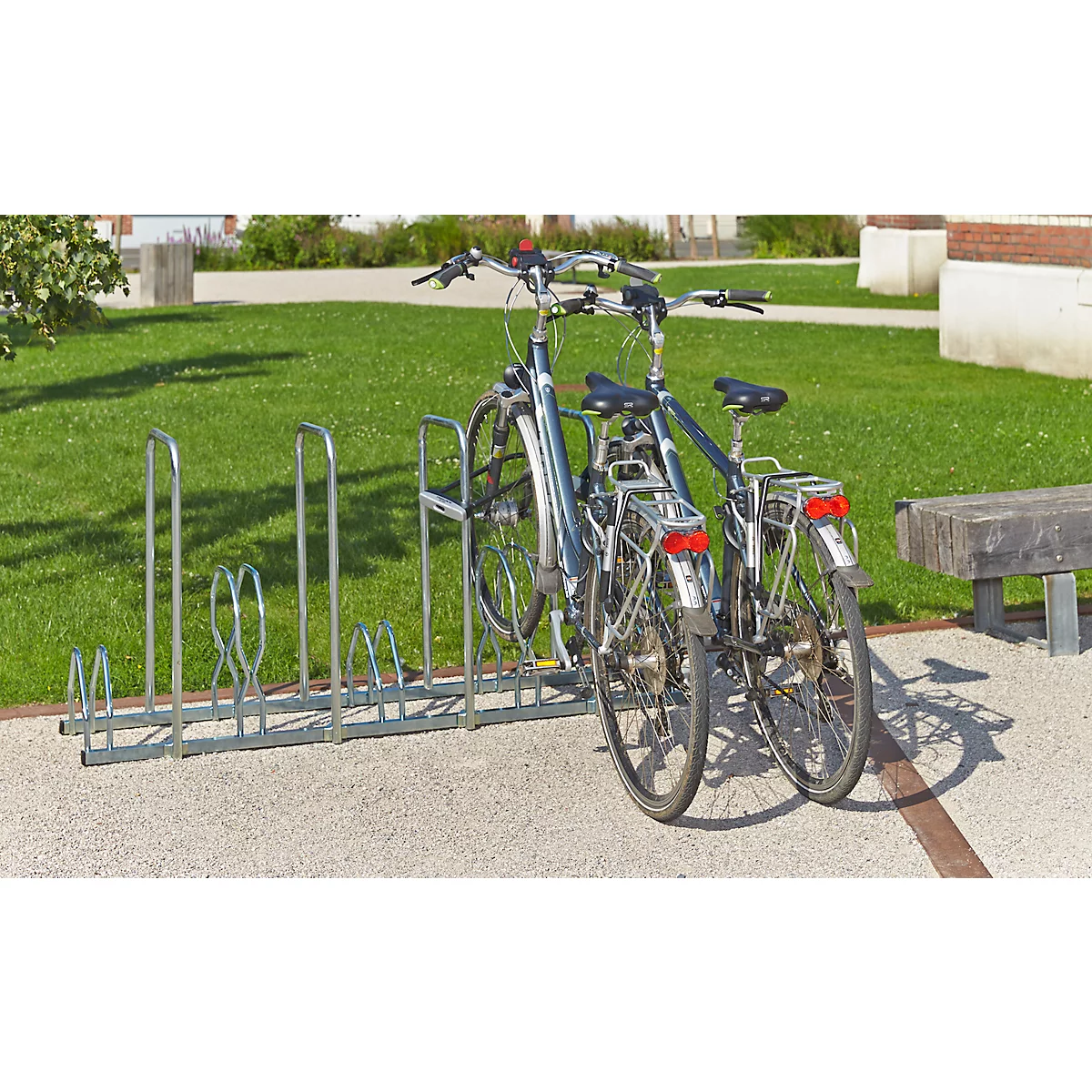 Twee fietsen in een fietsenrek op straatklinkers; daarachter een gazon en gebouwen.