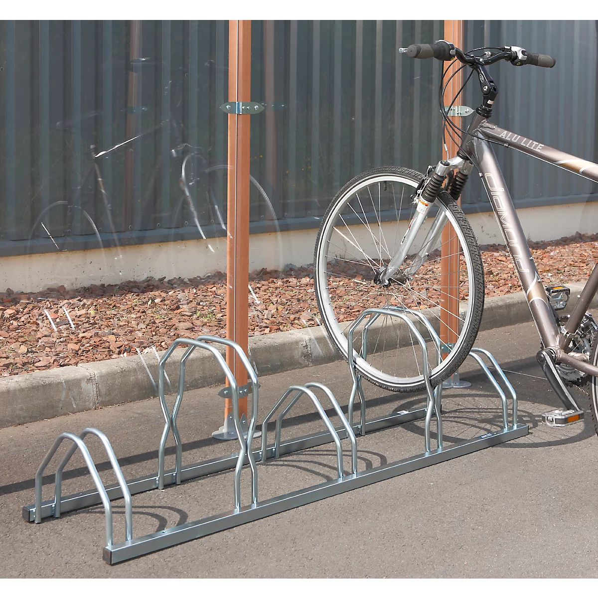 Fiets geparkeerd in een fietsenrek. Achter het rek staat een transparante wand en bruine steunen.