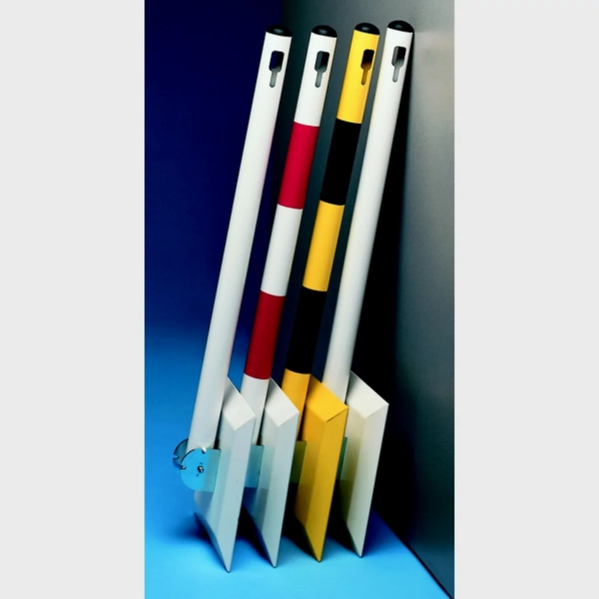 Mehrfarbige Pollerlehnen, die an einer grauen Wand stehen. Ein Poller hat rote und weiße Streifen, der andere gelbe und schwarze.