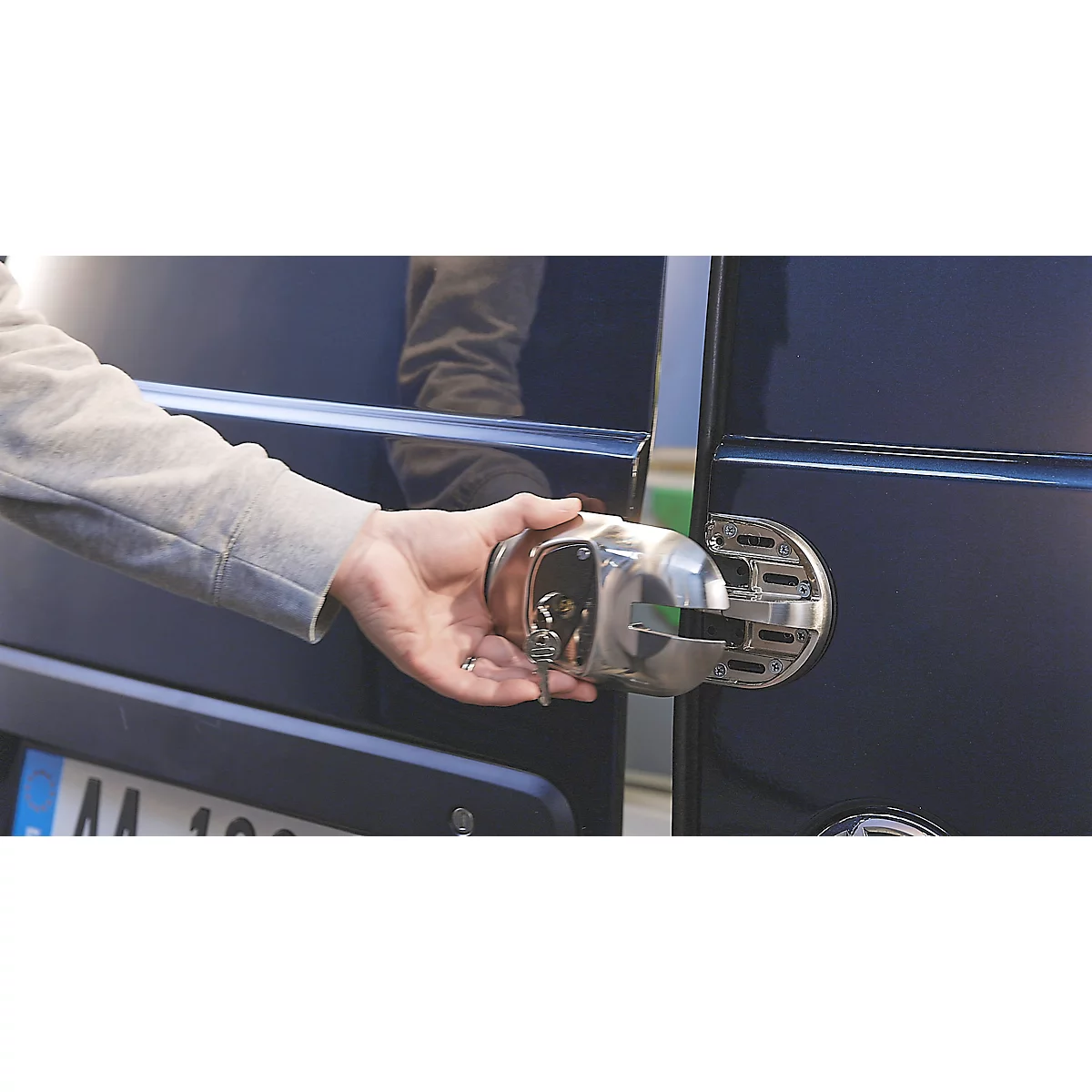 Een hand houdt een metalen slot voor een donkere voertuigdeur.