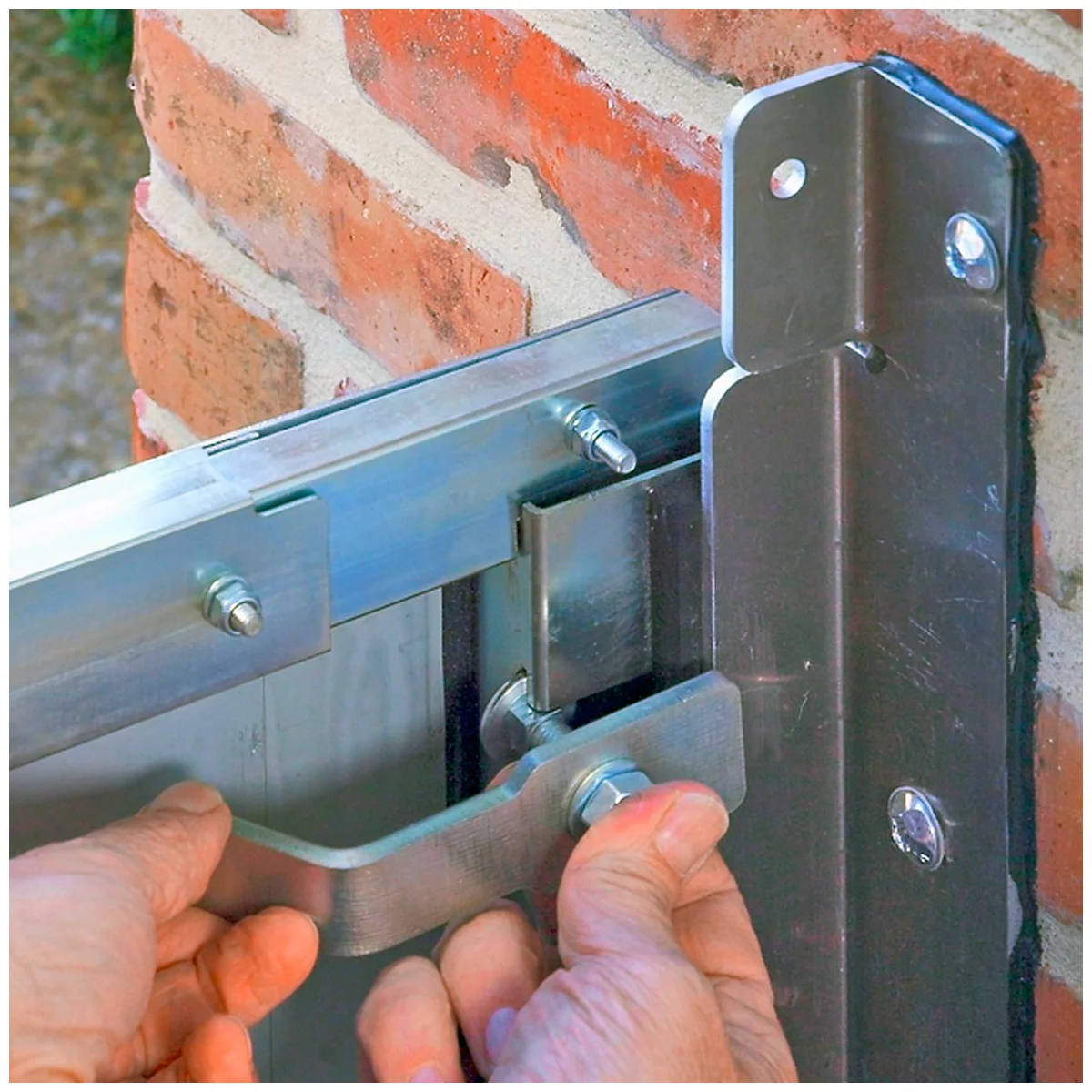 Handen houden metalen fitting op bakstenen muur. Fitting is op constructie geschroefd.