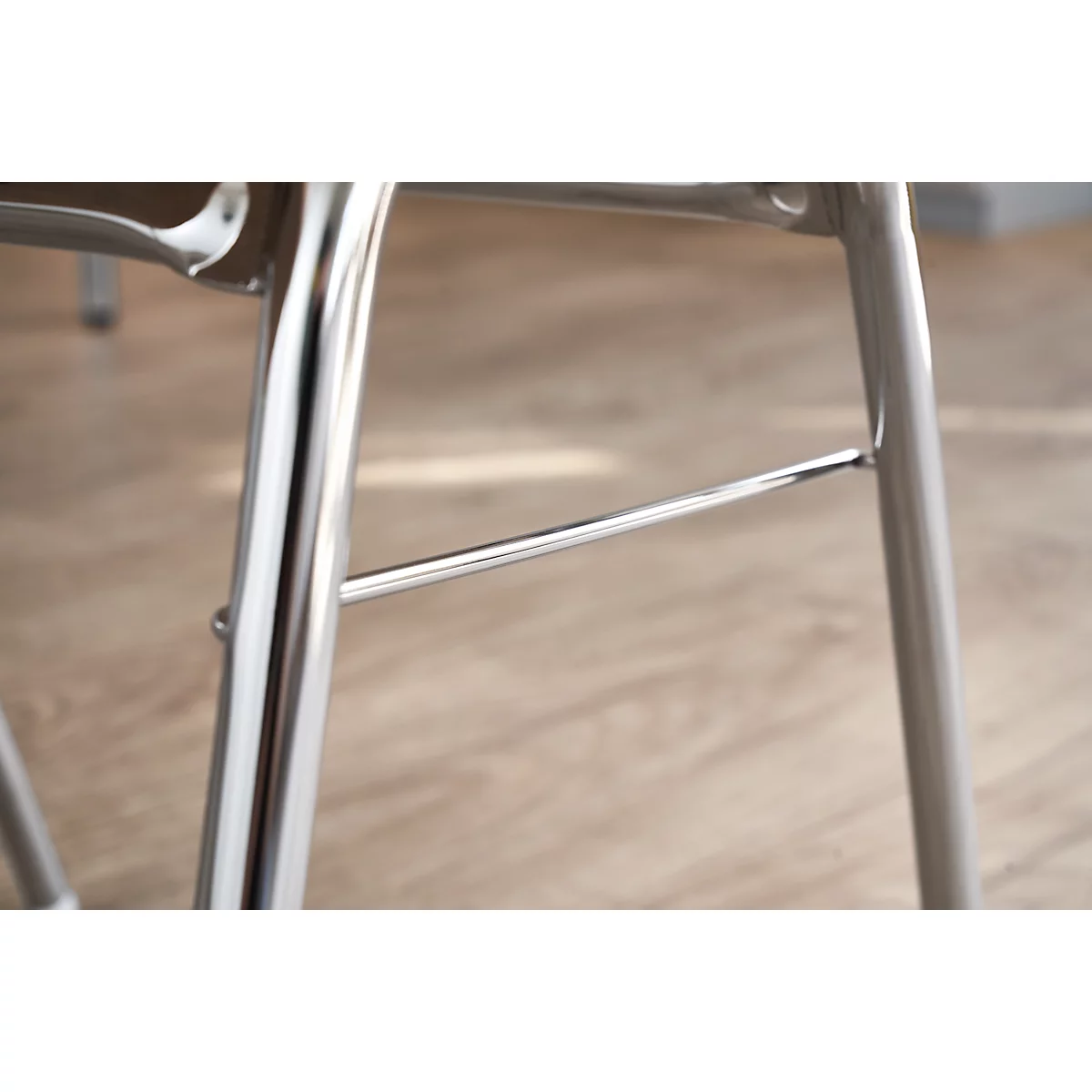 Close-up of the metal legs of a chair on light wood. The silver legs are stabilized by a bar.
