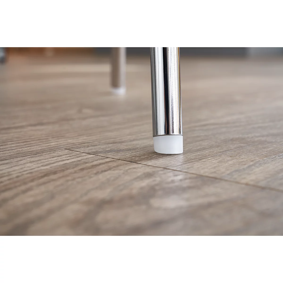 Close-up of a metal chair leg standing on a wooden floor. The leg has a light-colored plastic cap.