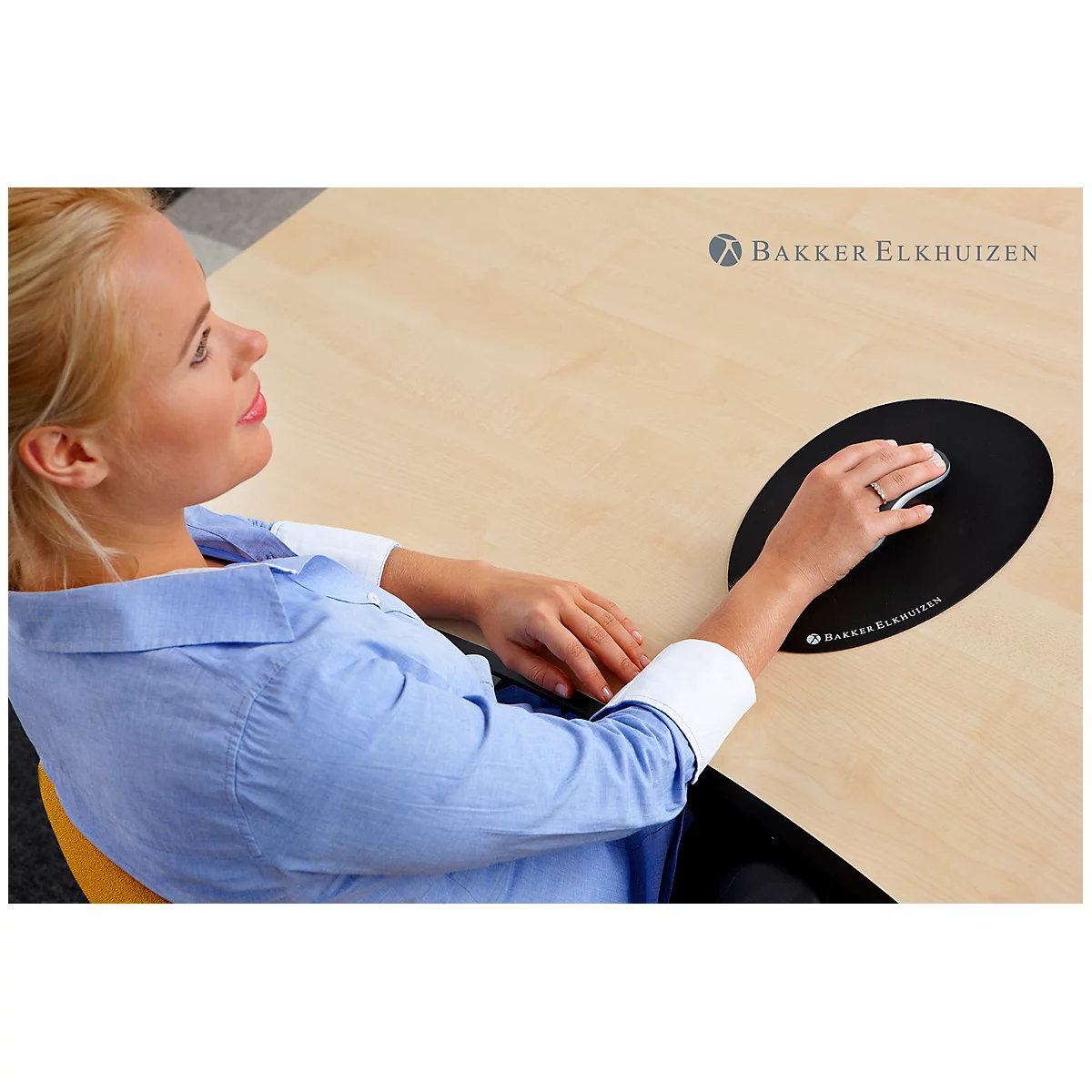 A woman sitting at a desk using a black ergonomic mouse. She is smiling while working.