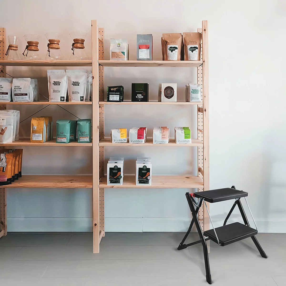 Étagères avec des produits de café, à côté d'un escabeau, devant un mur blanc.