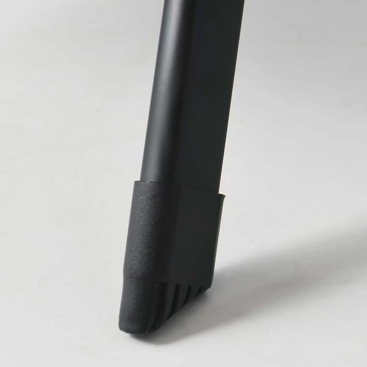 Gros plan sur un pied de chaise noir avec un dessous nervuré sur fond clair.