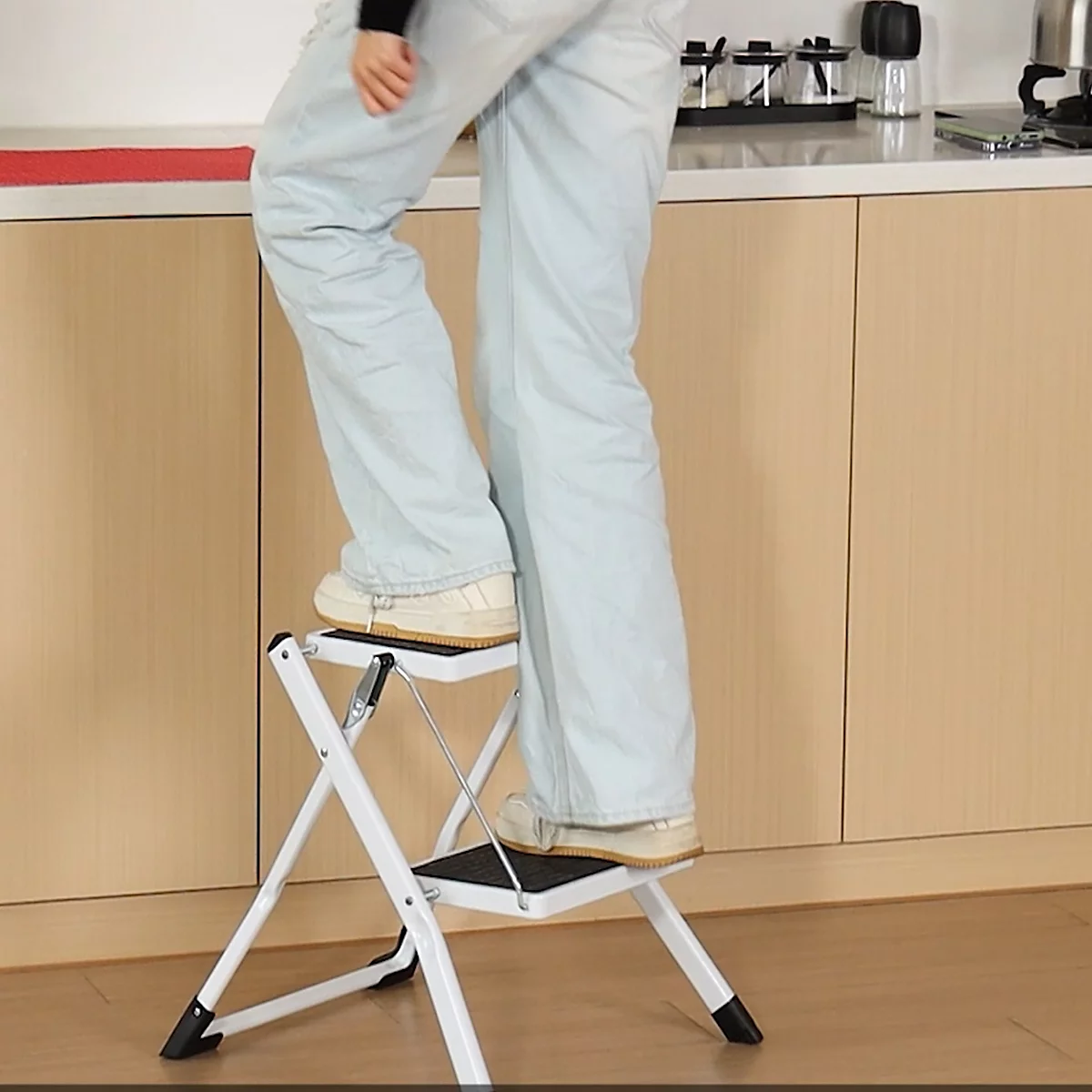 Une personne debout sur un escabeau blanc dans une cuisine. L'échelle est pliable.