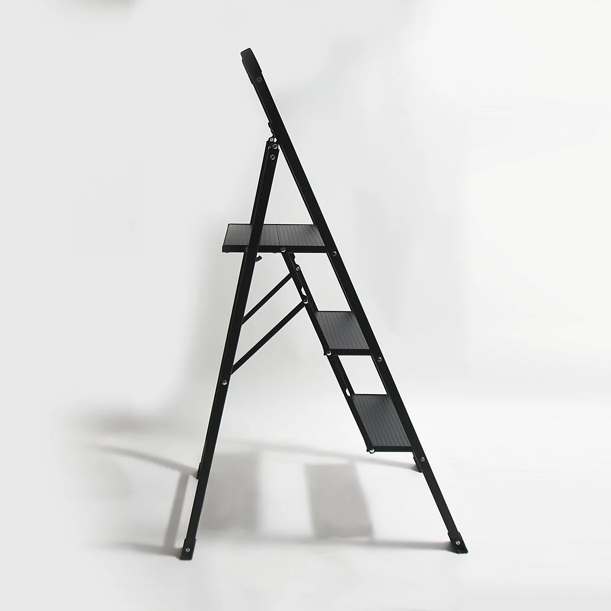 Un escabeau noir est positionné en diagonale sur un fond blanc. Il possède trois marches et un support.